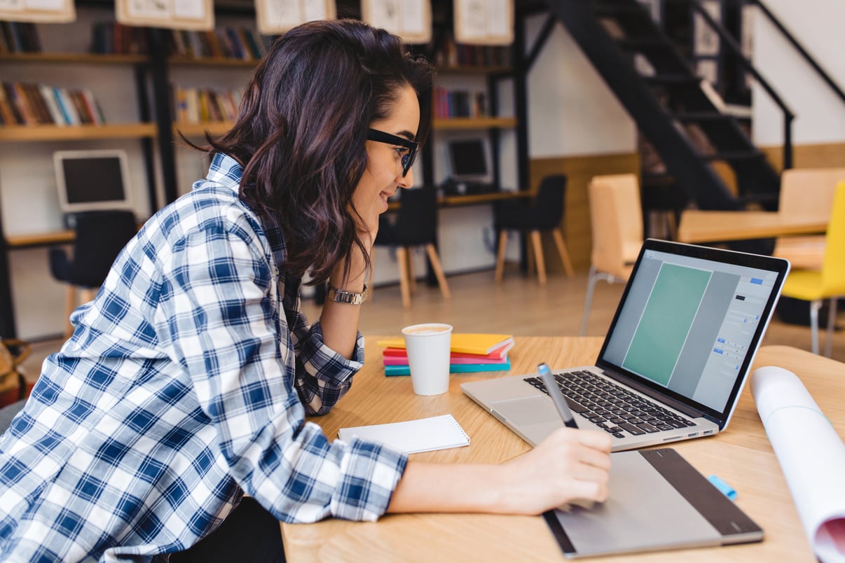 estudiar-momentos-mujer-joven-morena-muy-alegre-gafas-negras-trabajando-portatil-mesa-biblioteca-estado-animo-alegre-sonriente-diseno-trabajo-creativo-estudiante-inteligente-exito