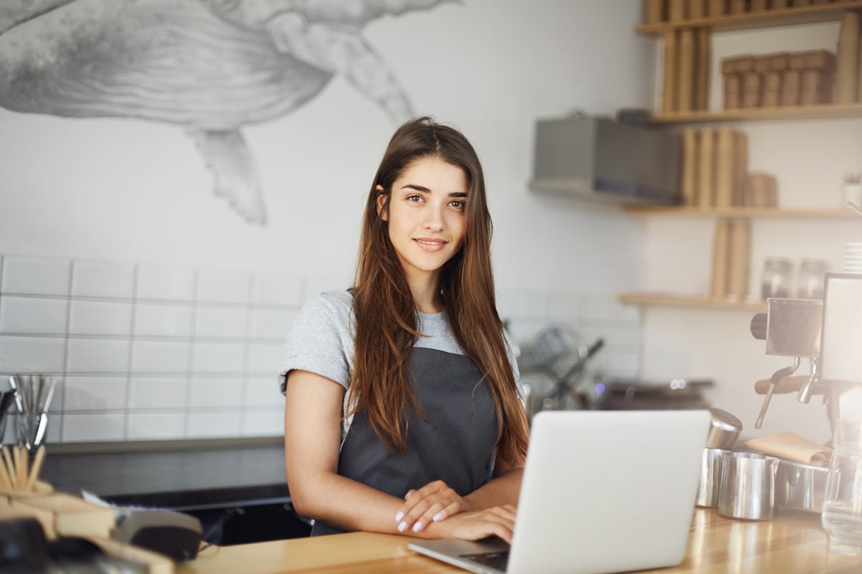 young-female-barista-using-laptop-computer-her-work-cafe-happy-employee-looking-camera-smiling